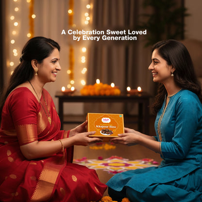 Two women exchanging a box of 'Khajoor Bite' with decorative lights and candles in the background.